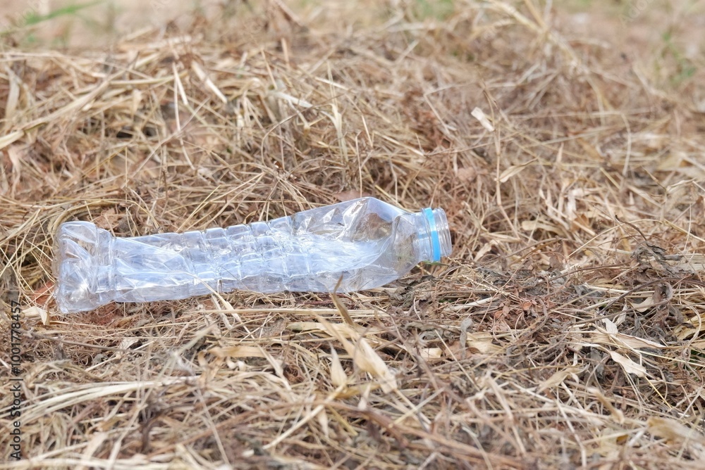 An empty of plastic drinking bottle littering on dried grass in outdoor for green environmental cleaning concept 