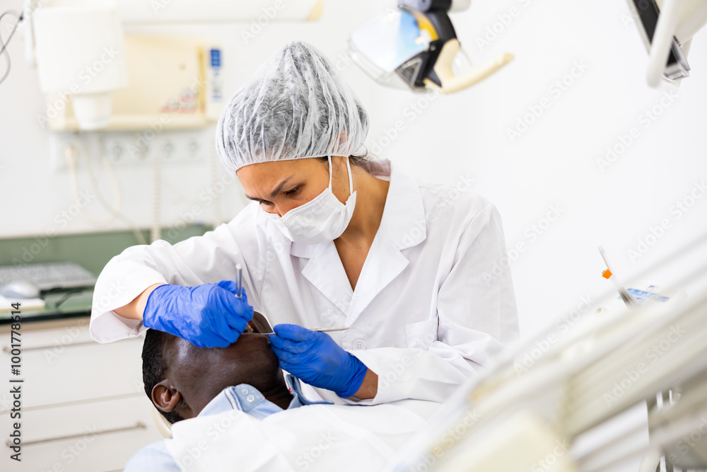 Naklejka premium Professional asian female dentist performing teeth treatment to adult african american man in dental clinic..
