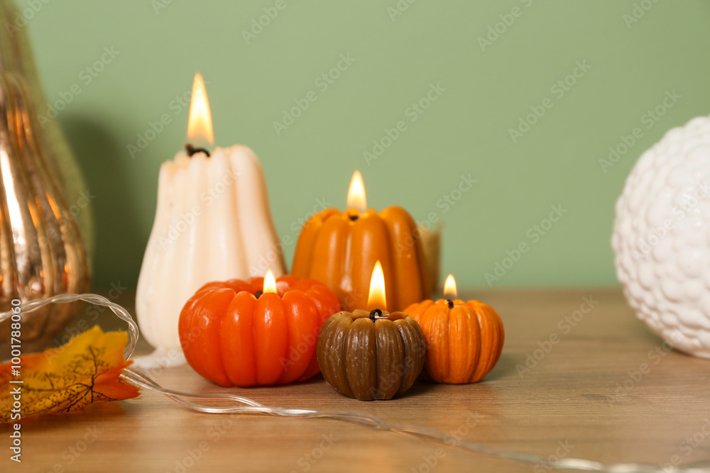 Burning candles in shape of pumpkins and autumn leaves on commode near green wall at home Burning candles in shape of pumpkins and autumn leaves on commode near green wall at home