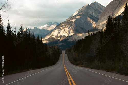 view of a road in the mountains going up and down with a tall mountain in the distance with light on it in fall photo