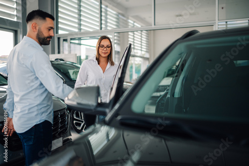 Obraz na płótnie Man assisting woman in entering modern vehicle at dealership