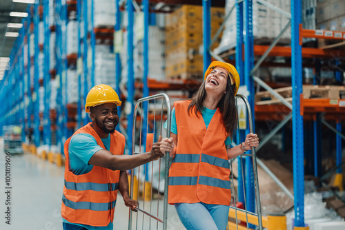 Fotografie Two multiracial warehouse workers having fun while pushing a handcart