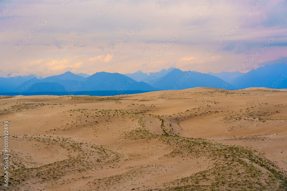 Expansive desert dunes under a dramatic sky with distant mountains Expansive desert dunes under a dramatic sky with distant mountains