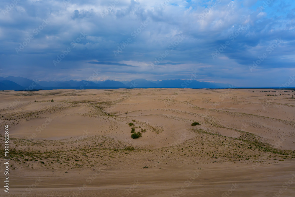 Expansive desert dunes under a dramatic sky with distant mountains Expansive desert dunes under a dramatic sky with distant mountains