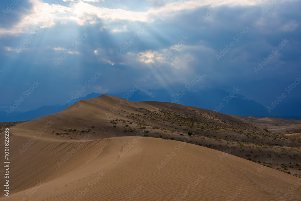 Dramatic desert dunes under sunbeams and cloudy sky Dramatic desert dunes under sunbeams and cloudy sky