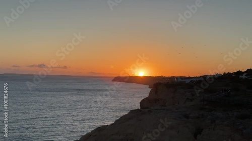 Sunset seen from Algar Seco, Carvoeiro, Algarve, Portugal. Suspension bridge over rock formations. Cliffs. Sunny day. Orange sky.
