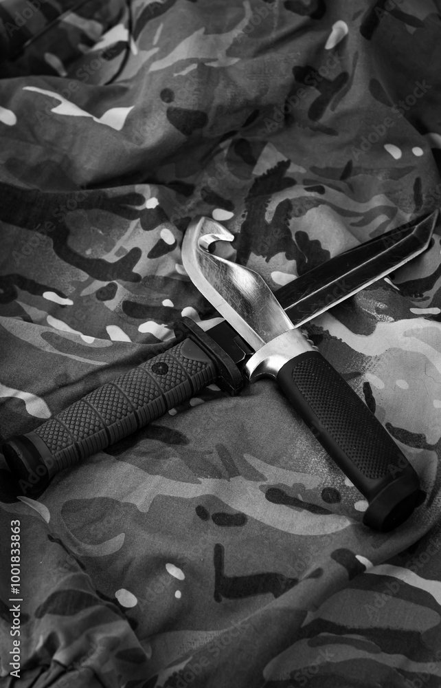 Naklejka premium Two fixed stainless steel knives crossed with each other, a tourist one with a black handle and a military one with a green handle, on a pixelated background. Black and white vertical photo, top down.