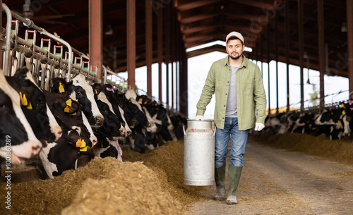 Male farmer carries a large milk can in his hands at a cow farm photo