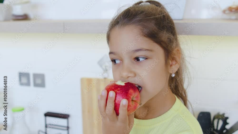 A joyful young girl is happily enjoying a fresh, delicious apple while being in her cozy kitchen, radiating a sense of contentment and delight as she savors the taste of the fruit A joyful young girl is happily enjoying a fresh, delicious apple while being in her cozy kitchen, radiating a sense of contentment and delight as she savors the taste of the fruit