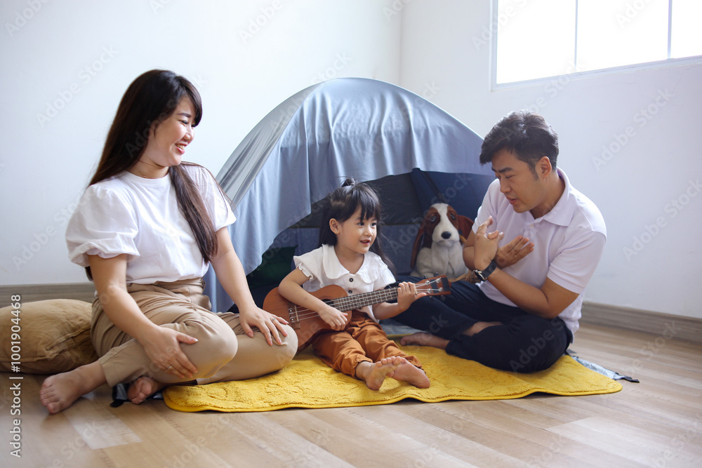 Joyful Asian Little Girl Playing Ukulele With Parents While Sitting on Floor at Tent Joyful Asian Little Girl Playing Ukulele With Parents While Sitting on Floor at Tent