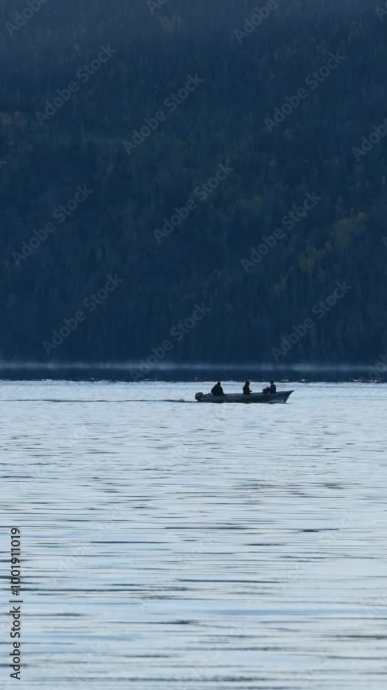 A small motor boat with three passangers floats across a mountain lake on cold fall evening boardering a forest during blue hour. A small motor boat with three passangers floats across a mountain lake on cold fall evening boardering a forest during blue hour.