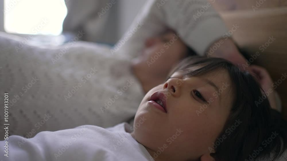 Mother and young boy lying in bed, with the mother peacefully asleep and the boy with pensive expression, capturing a quiet and intimate family moment, perfect for lifestyle Mother and young boy lying in bed, with the mother peacefully asleep and the boy with pensive expression, capturing a quiet and intimate family moment, perfect for lifestyle