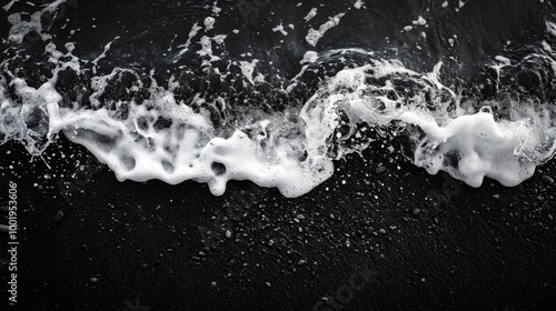 A close-up shot of a wave breaking on a black sand beach, with the dark sand contrasting sharply with the white foam of the wave