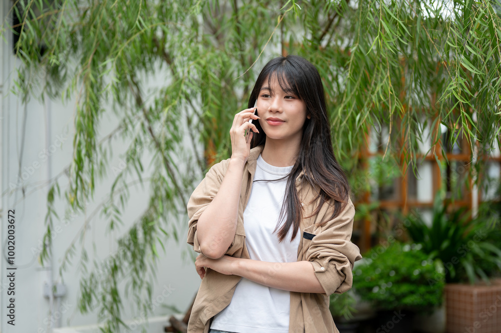 A charming young Asian woman is talking on the phone while walking through her home garden. A charming young Asian woman is talking on the phone while walking through her home garden.