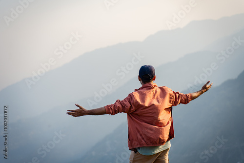 Young man standing with open arms on a mountain peak himachal pradesh india.
