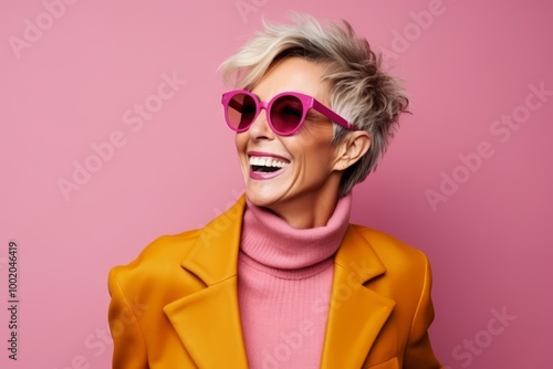 Fashionable woman in yellow coat and pink sunglasses on pink background