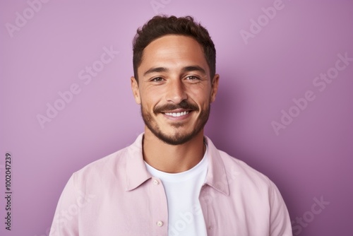 Portrait of handsome young man looking at camera and smiling while standing against purple background