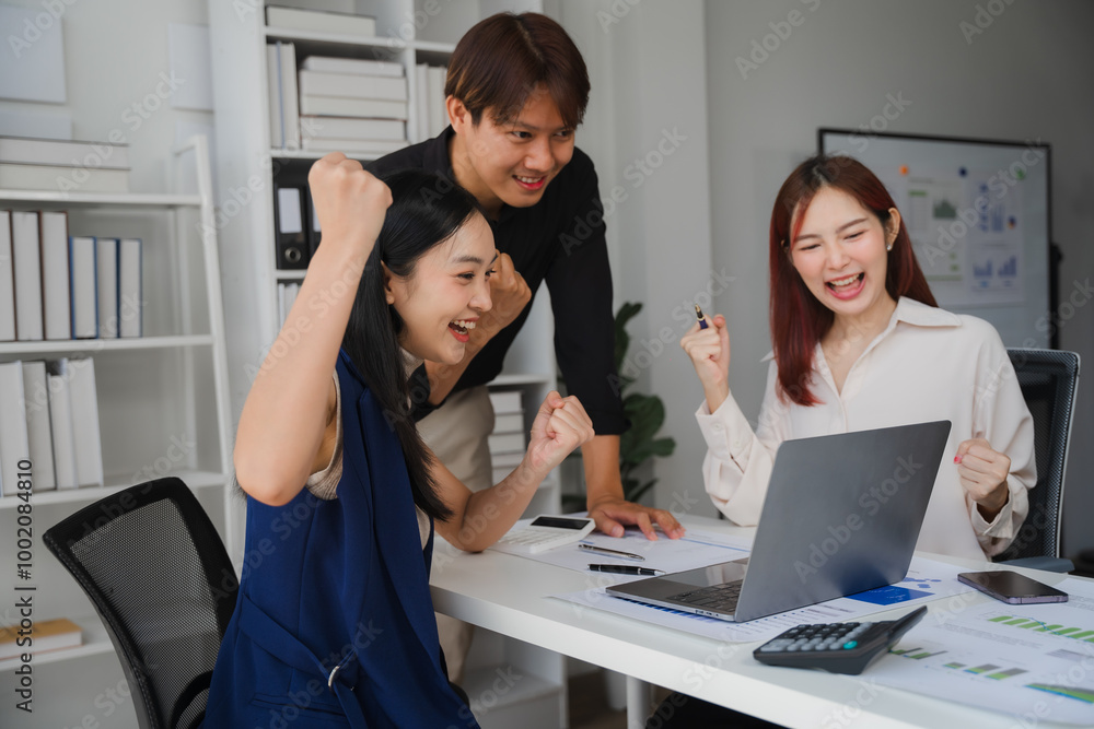 Business Success: A diverse team of three young Asian business professionals celebrates a big win at their office desk, showing off their excitement and joy. Business Success: A diverse team of three young Asian business professionals celebrates a big win at their office desk, showing off their excitement and joy.