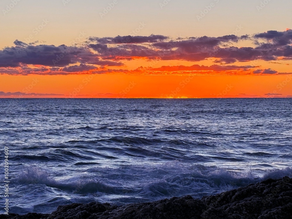 Naklejka premium Sunset clouds over sea waves and rocky coast. 