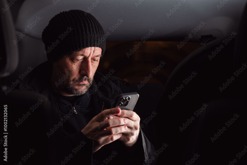 Adult caucasian male reading text message on cellular phone while sitting at the back seat of the car at night Adult caucasian male reading text message on cellular phone while sitting at the back seat of the car at night