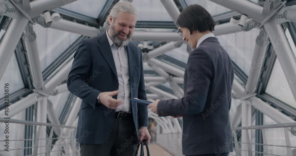 Two businessmen Asian and Caucasian standing in modern glass hall talking and shaking hands discussing business. Cooperation and people concept. Two businessmen Asian and Caucasian standing in modern glass hall talking and shaking hands discussing business. Cooperation and people concept.