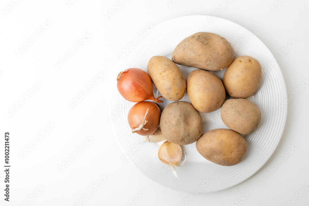 A white plate with fresh potatoes, onions, and garlic, ideal ingredients for traditional Thanksgiving dinner preparations A white plate with fresh potatoes, onions, and garlic, ideal ingredients for traditional Thanksgiving dinner preparations