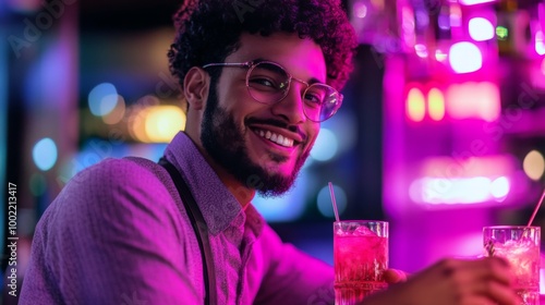 Man with curly hair smiling and holding a pink drink at a bar with neon lights photo