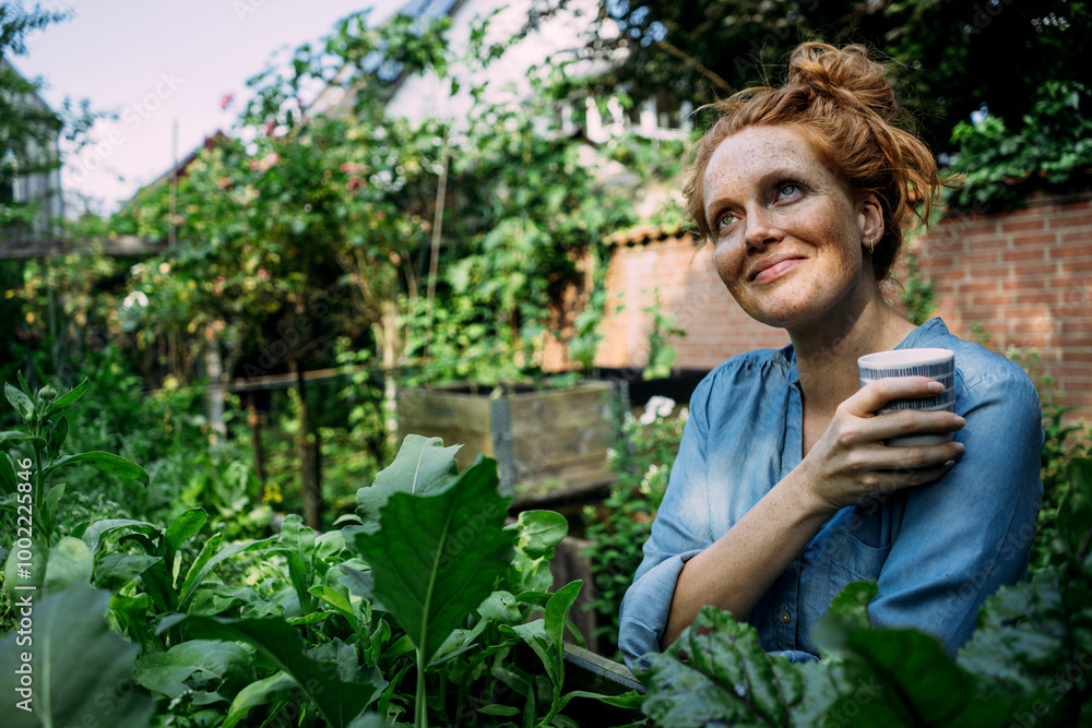 Smiling woman with coffee cup near plants in back yard Smiling woman with coffee cup near plants in back yard