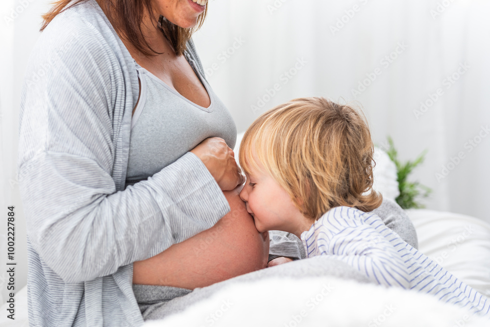 Blond boy kissing pregnant mother's belly at home Blond boy kissing pregnant mother's belly at home
