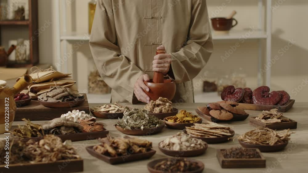 A doctor in brown traditional using a wood mortar and pestle to attire grinds dried herbs, surrounding are other herbal ingredients in a traditional laboratory setting for traditional medicine videos A doctor in brown traditional using a wood mortar and pestle to attire grinds dried herbs, surrounding are other herbal ingredients in a traditional laboratory setting for traditional medicine videos