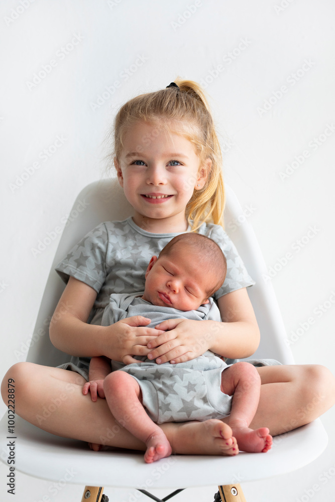Smiling blond girl sitting with baby brother on chair Smiling blond girl sitting with baby brother on chair