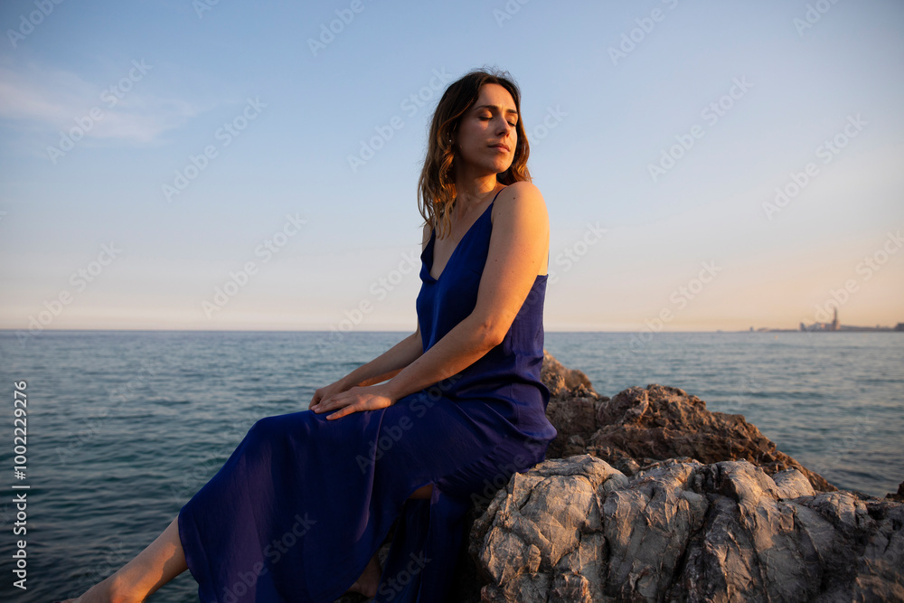 Beautiful woman with eyes closed sitting on rock near sea Beautiful woman with eyes closed sitting on rock near sea