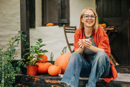 Smiling woman with eyeglasses holding coffee cup sitting on porch