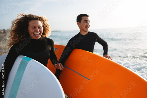 Photography Beautiful happy surfer couple having fun on the beach, running with surfboard to