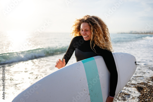 Photography Joyful young woman carrying a surfboard on a beach, her face filled with happine