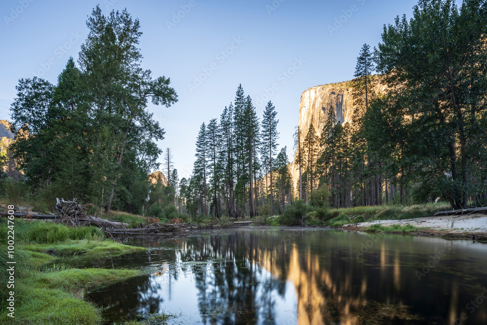View of the towering granite monolith of El Capitan, in Yosemite National Park, at sunrise, with the Merced river flowing in the foreground, reflecting the cliff face. View of the towering granite monolith of El Capitan, in Yosemite National Park, at sunrise, with the Merced river flowing in the foreground, reflecting the cliff face.
