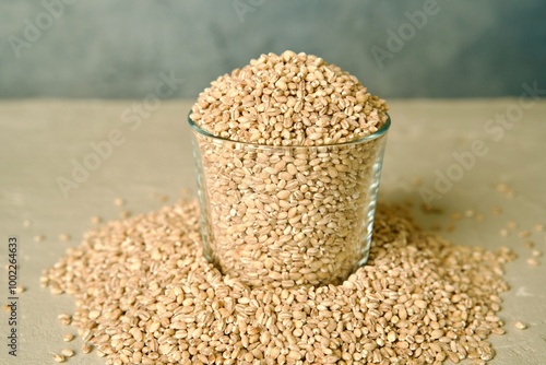 A glass jar filled with pearl barley, with scattered barley grains around it on a light surface. photo