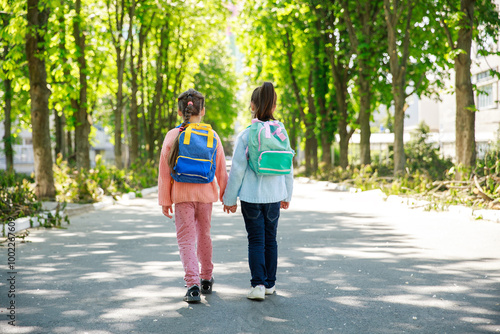 Two young girls stroll down a picturesque avenue, hand in hand, surrounded by vibrant greenery. Their colorful backpacks hint at the adventures that await them.