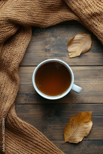 Cozy cup of tea surrounded by a sweater and spices on wooden table