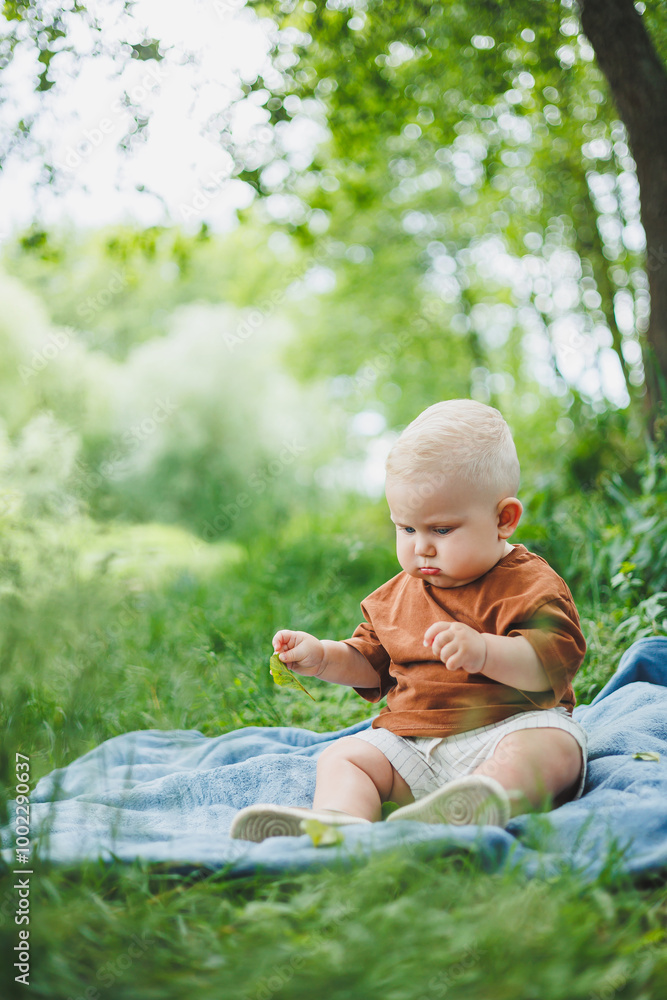 A blond toddler in a t-shirt and shorts sits on the green grass and plays. A child is playing on the street. The baby sits independently. A blond toddler in a t-shirt and shorts sits on the green grass and plays. A child is playing on the street. The baby sits independently.