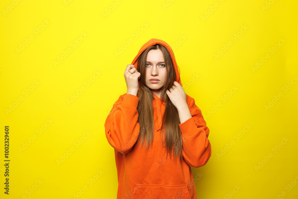 Young woman in orange hoodie on yellow background. Sad face, posing for camera, copy space. Young woman in orange hoodie on yellow background. Sad face, posing for camera, copy space.