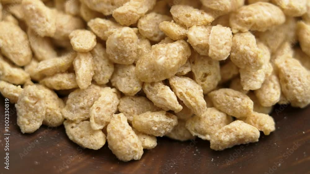 Crunchy wholegrain flakes with a rich texture and bold cereal flavour falling into a wooden brown bowl for organic morning breakfast. Macro. Rotation Crunchy wholegrain flakes with a rich texture and bold cereal flavour falling into a wooden brown bowl for organic morning breakfast. Macro. Rotation