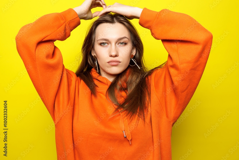 Young woman posing in orange hoodie on yellow background. Young woman posing in orange hoodie on yellow background.