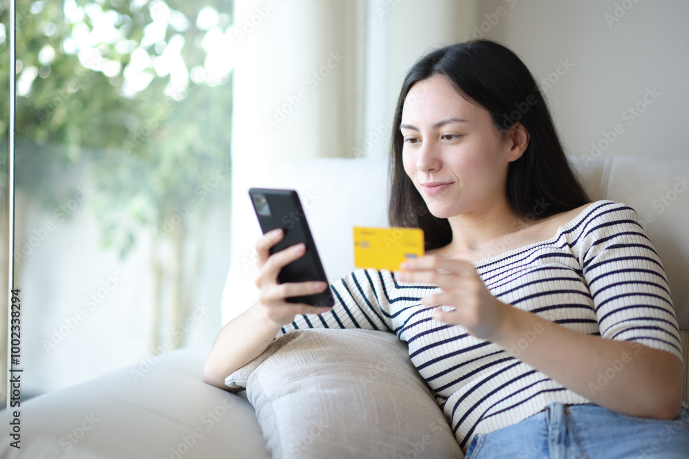 Serious asian woman buying online with card and phone at home Serious asian woman buying online with card and phone at home