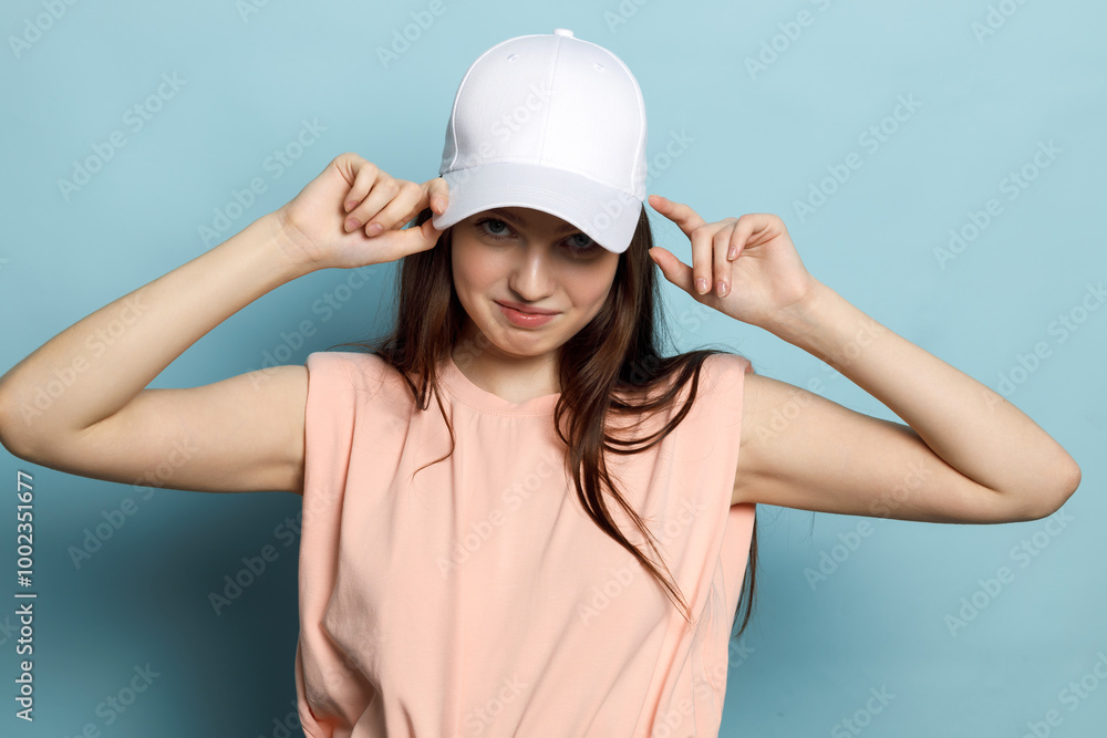 Young woman, teenager, model, posing in white cap and pink T-shirt on blue background. Sweet face, smiling, laughing. Young woman, teenager, model, posing in white cap and pink T-shirt on blue background. Sweet face, smiling, laughing.