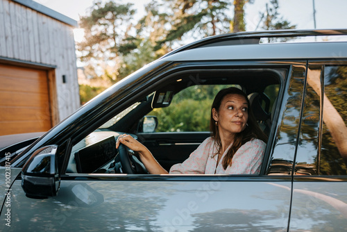 Mature woman looking over shoulder while reversing car on driveway