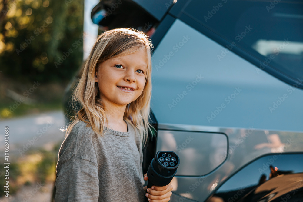 Portrait of smiling boy with blond hair holding electric plug near car at charging station Portrait of smiling boy with blond hair holding electric plug near car at charging station