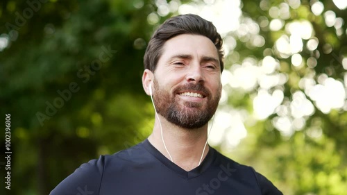 Happy joyful athlete relaxing with closed eyes standing in urban city park. Smiling handsome bearded runner breathes deeply and enjoys being in nature while resting after a morning workout. Close up