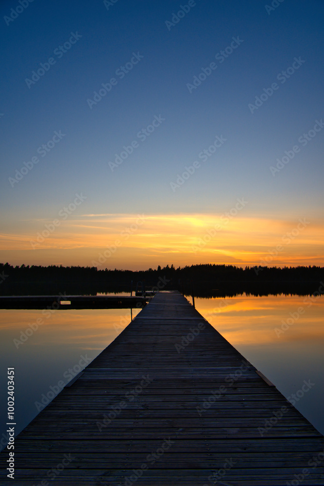 Naklejka premium Wooden jetty at sunset on a Swedish lake. Sunset reflected in the water