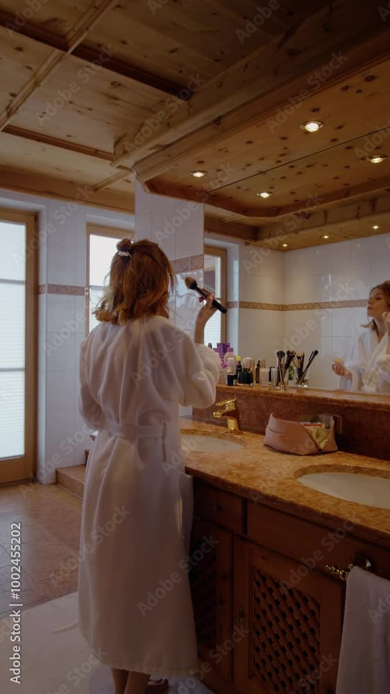 Vertical Screen: Female in bathrobe arranging hair in the mirror. Woman getting ready for date fixing her hair style.
